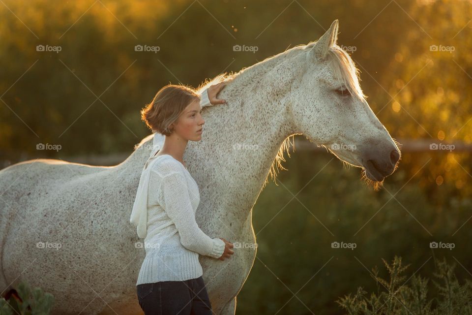Teen girl with her horse in a farm at sunset