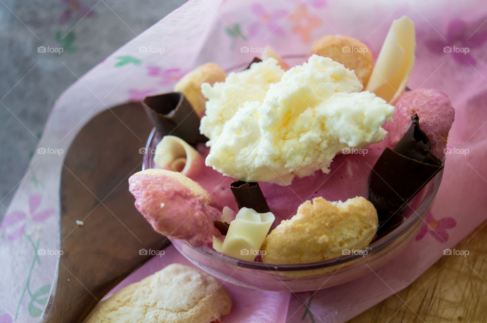 Making Vanilla and Strawberry Ice Cream Charlotte dessert with homemade lady fingers and dark chocolate in glass bowl on pink background with wooden spoon conceptual classic variations epicure photography