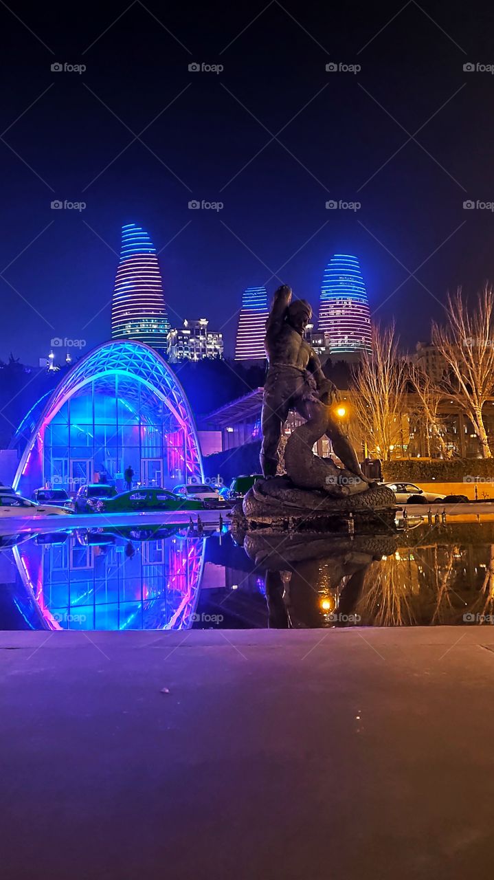 Monument to Azerbaijani hero Bahramgur killing the dragon with flame tower background night view