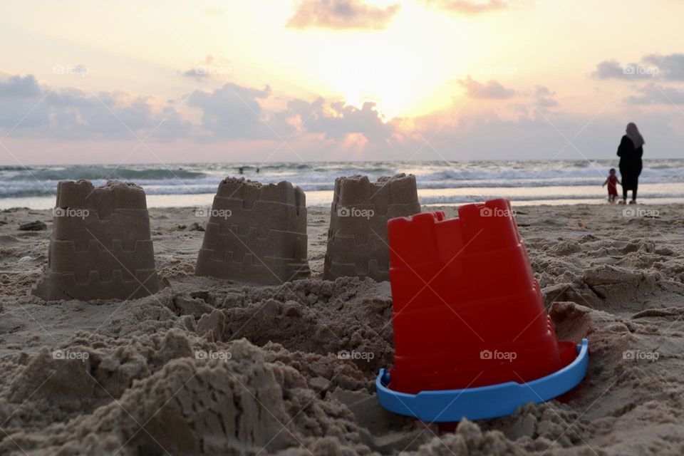 Sand castles with red bucket at sunset on the beach 