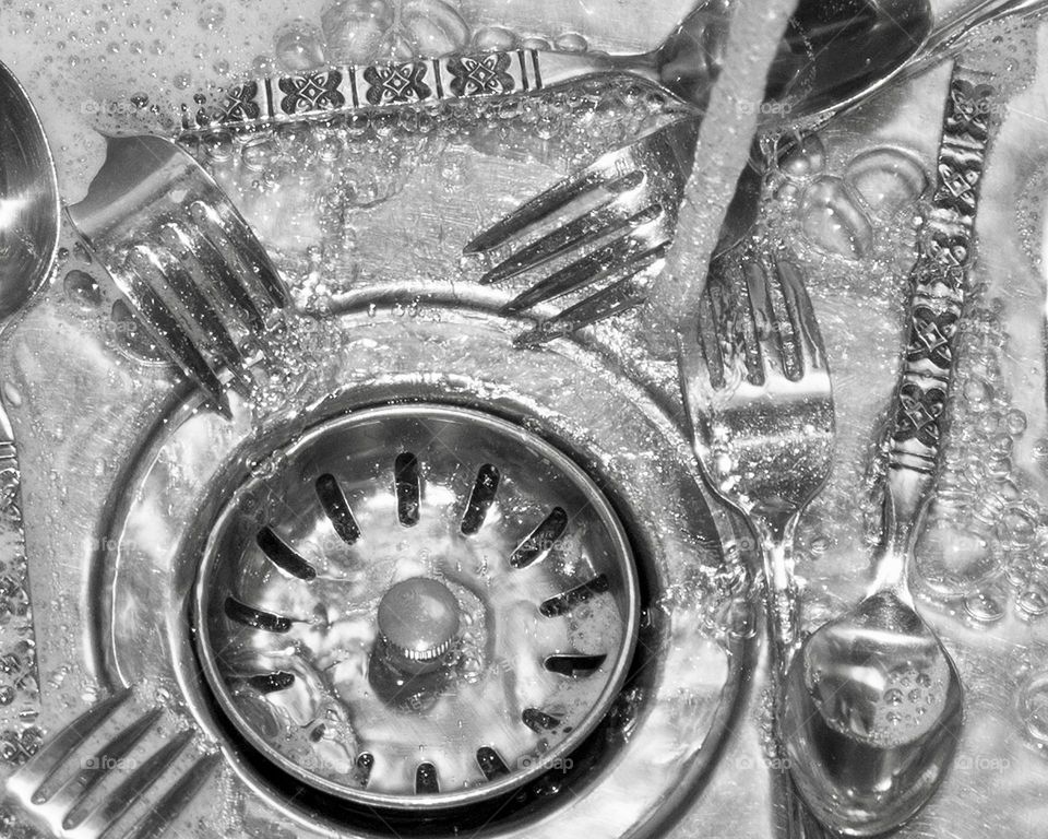 Silverware in the sink with running water 