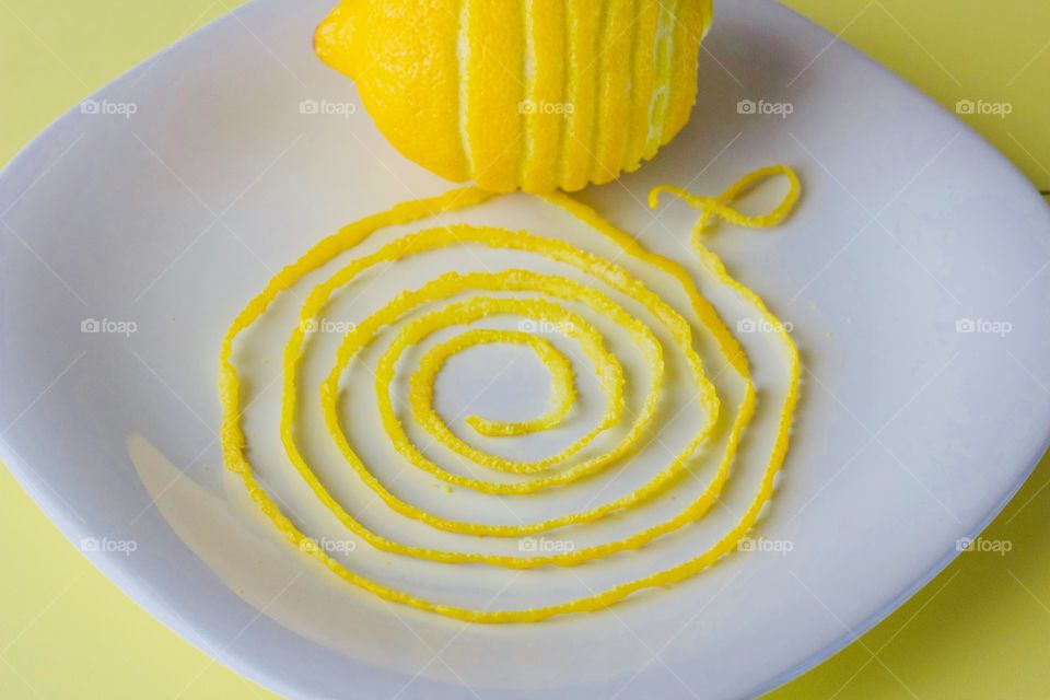 Lemon and spiraled lemon peel on a white plate with yellow background  