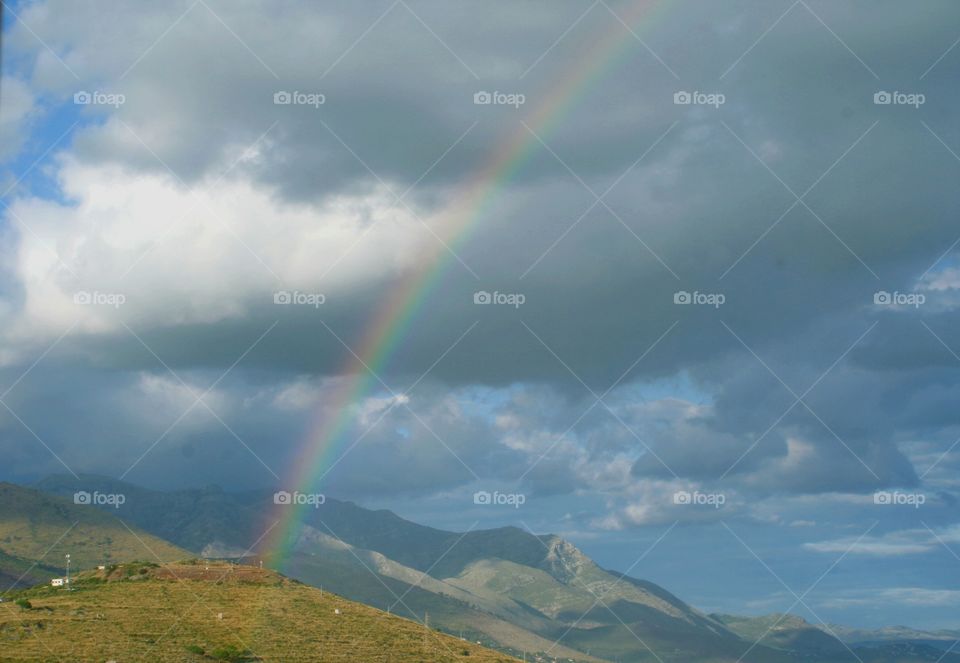 Rainbow between clouds and hills