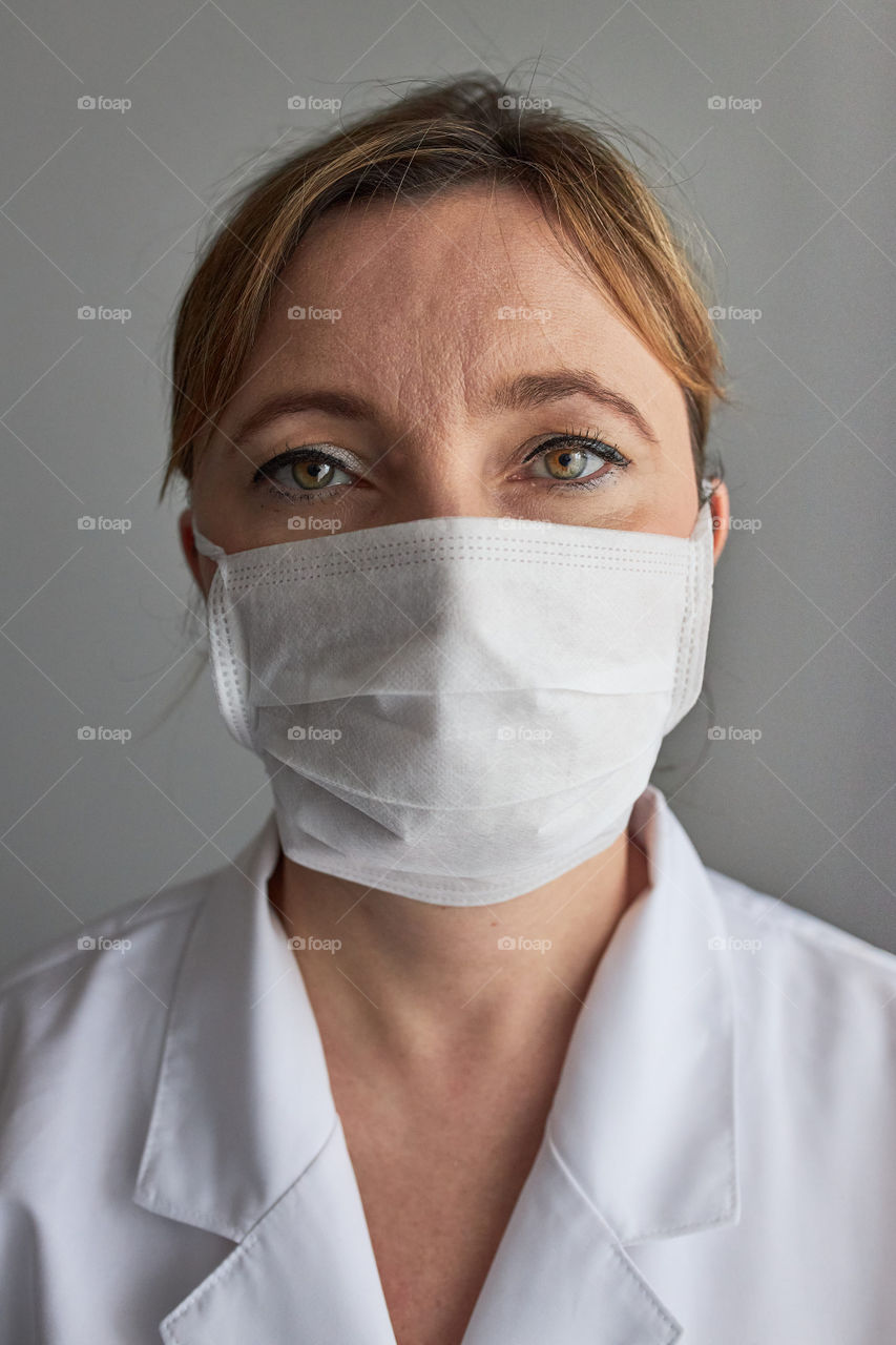 Doctor with face covered with mask. Portrait of young woman wearing the uniform, cap and mask to avoid virus infection and to prevent the spread of disease. Real people, authentic situations