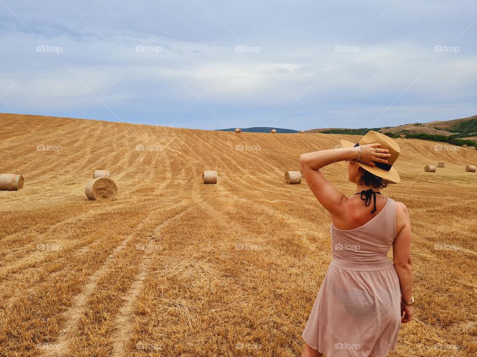woman from behind with straw hat in a summer golden wheat field