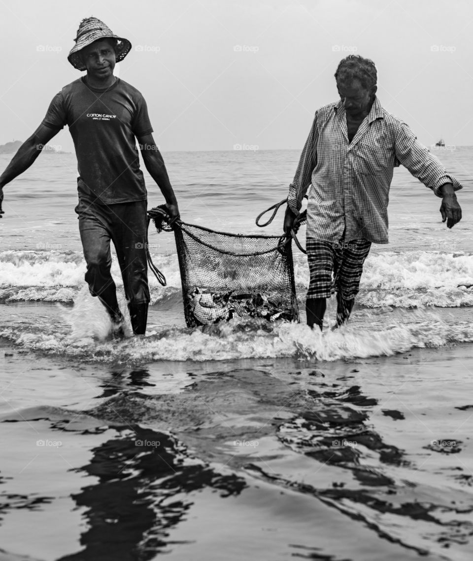 monochrome image of fishermen coming out of sea with a net full of 🐟 fish !! 🙂