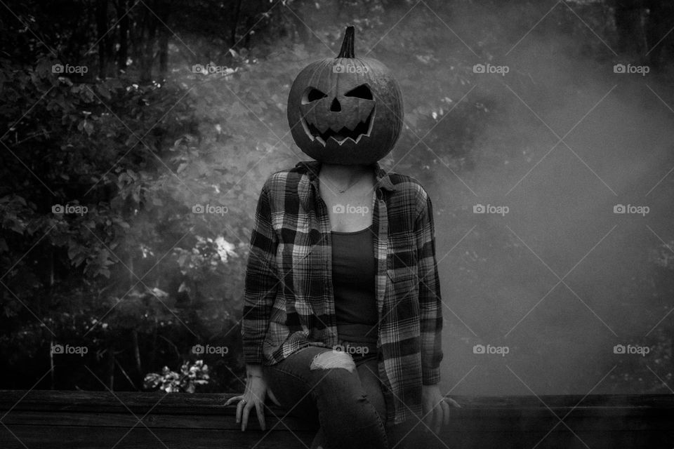 Black and White for a eerie mood; Woman outdoors with a carved pumpkin and fog