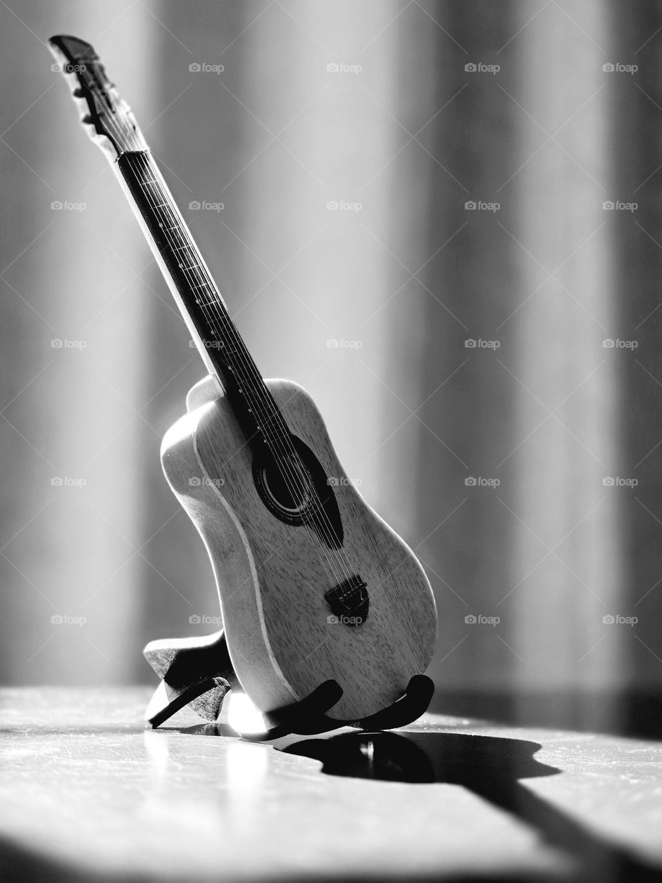 Small collection guitar placed on a table while receiving sunlight on it, in monochrome style.