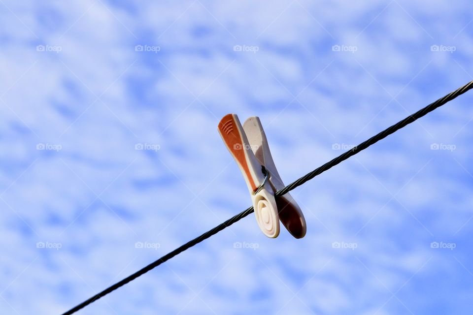 Single clothes pegs clothespin on a laundry line outdoors against a cloudy blue sky