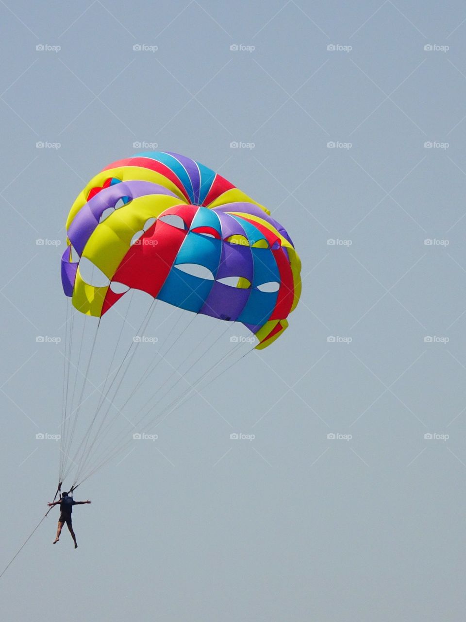 man is up in the air with a colorful parachute in summer