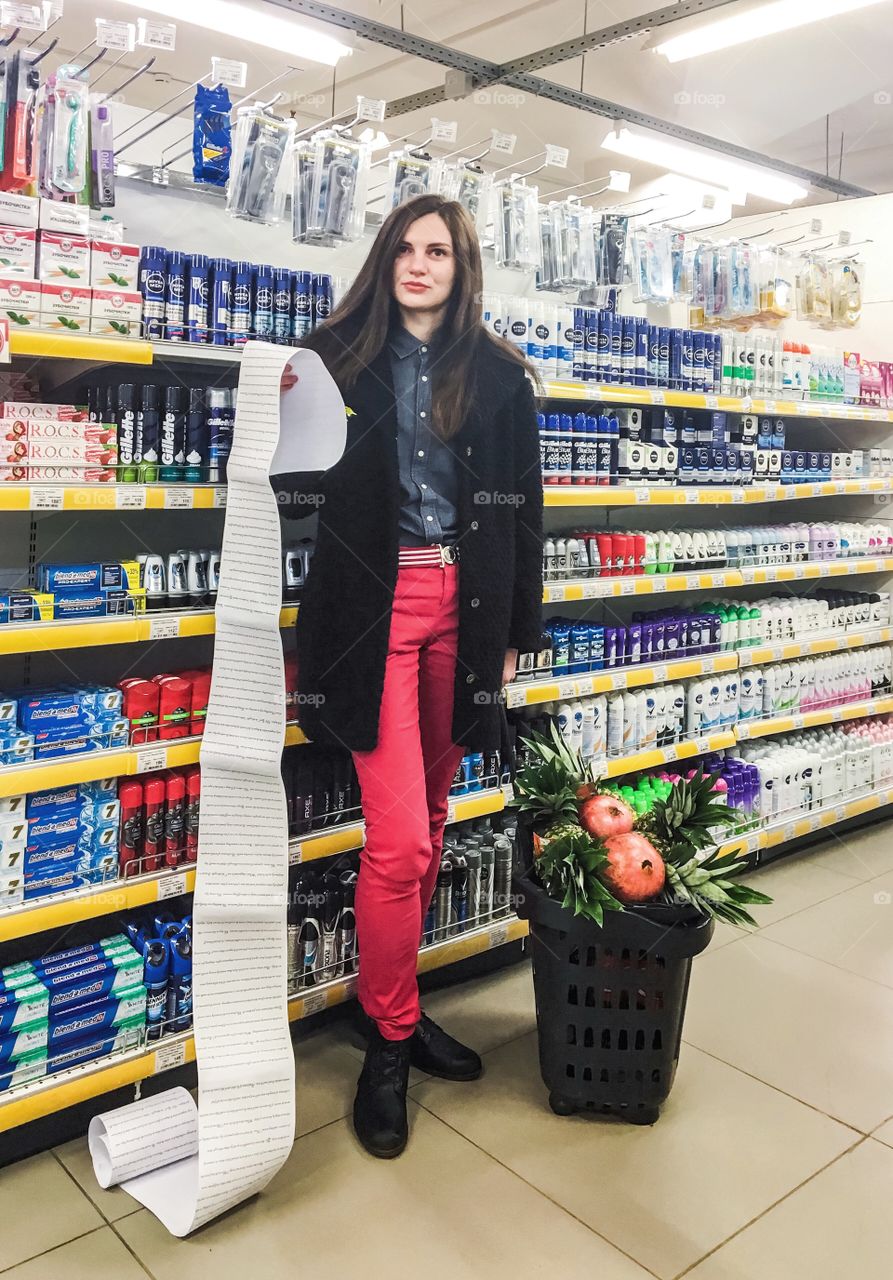 Girl running errands with super long shopping list in grocery store with pomegranates and pineapples  in cart