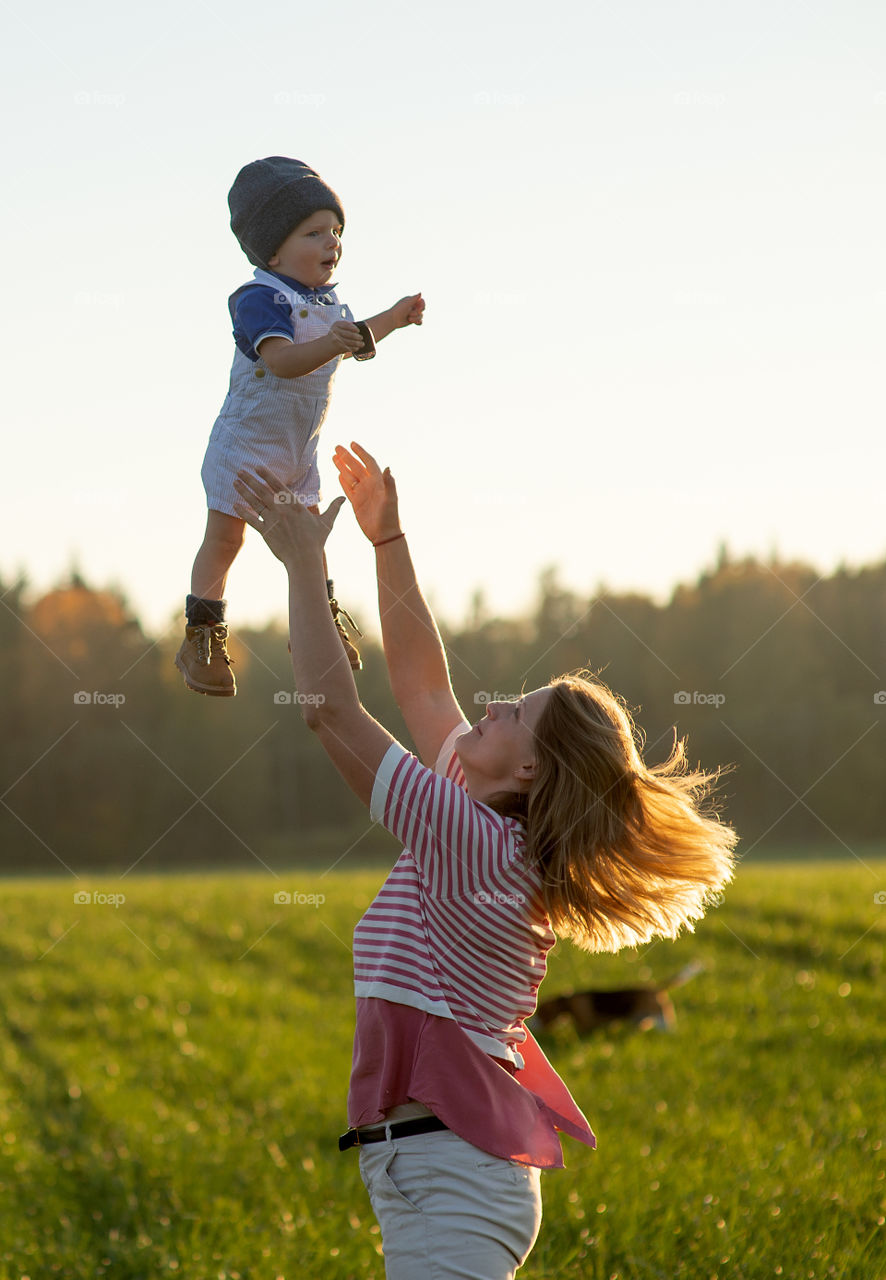 Happy harmonious family outdoors. Mother throws baby up, laughing and playing in the summer on the nature