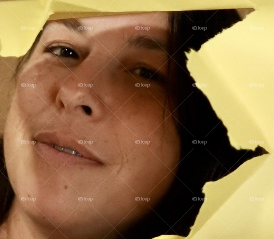 Face skin in the forties of a woman with freckles and brown hair seen through a broken yellow paper.