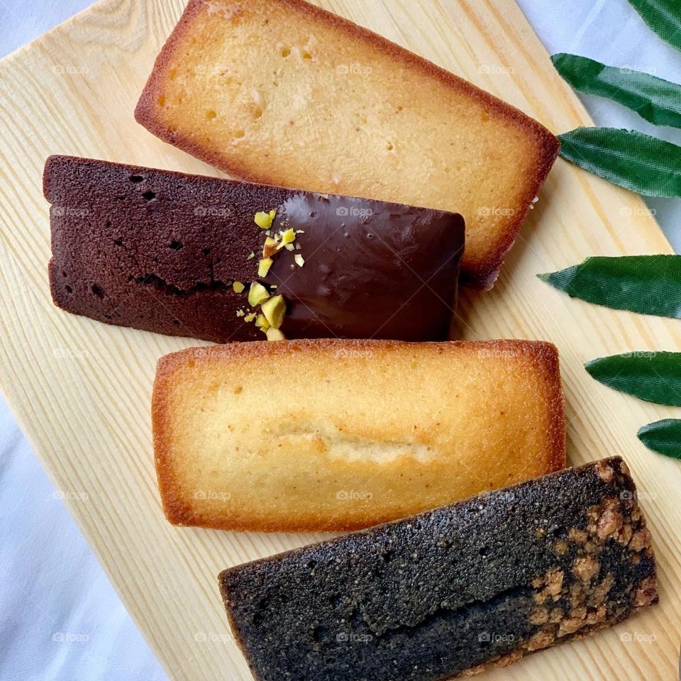 French patisserie financiers in four different flavours - brown butter, dark chocolate, black sesame and yuzu against a natural background 