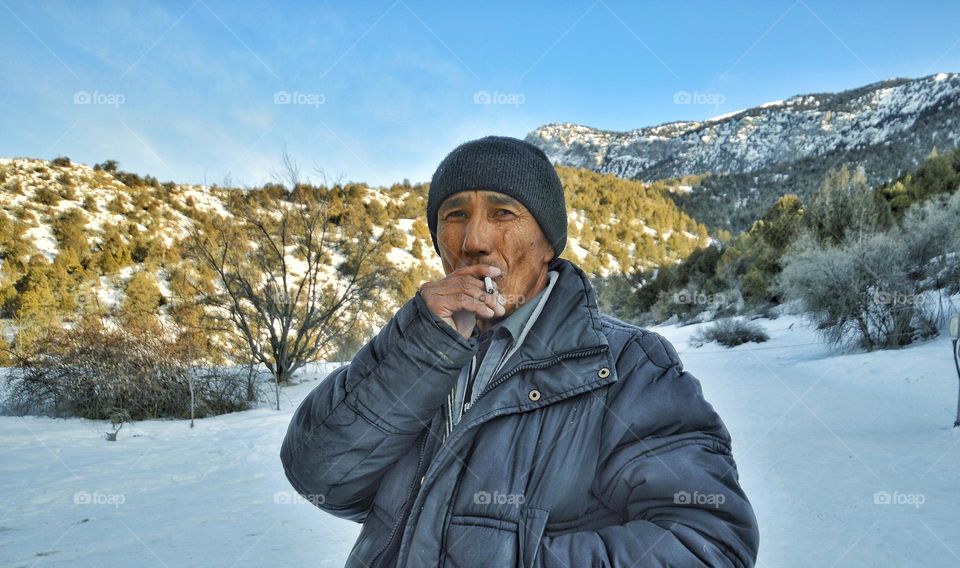 not a young man with a cigarette stands against the backdrop of mountains in early spring