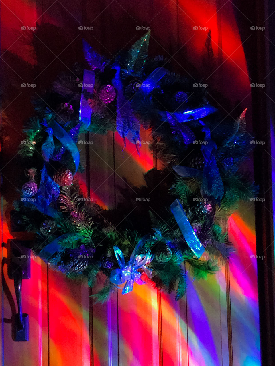 Night: A nighttime photo of our Christmas peacock themed wreath on our beautiful wood door. The kaleidoscope strobe light rhythmically swirls multi coloured light across the festive entranceway. 