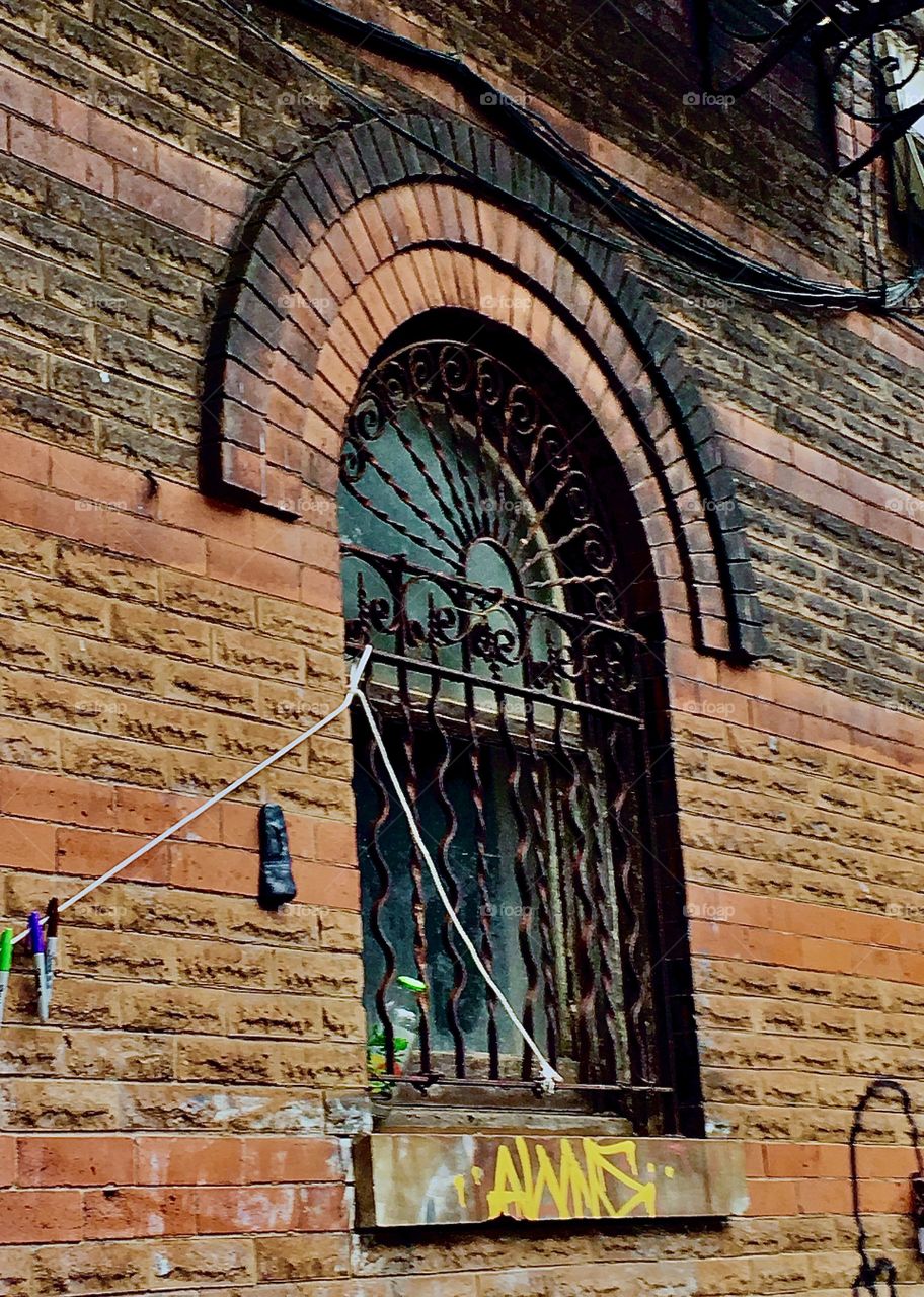 Side view of the abandoned brownstone built in the 1890s in the style of the „Victorian Age“ with iron cast ornamented bars in front of the arched 2nd story window in Fort Greene, Bklyn. Photo from 2020. Hypnotic Productions