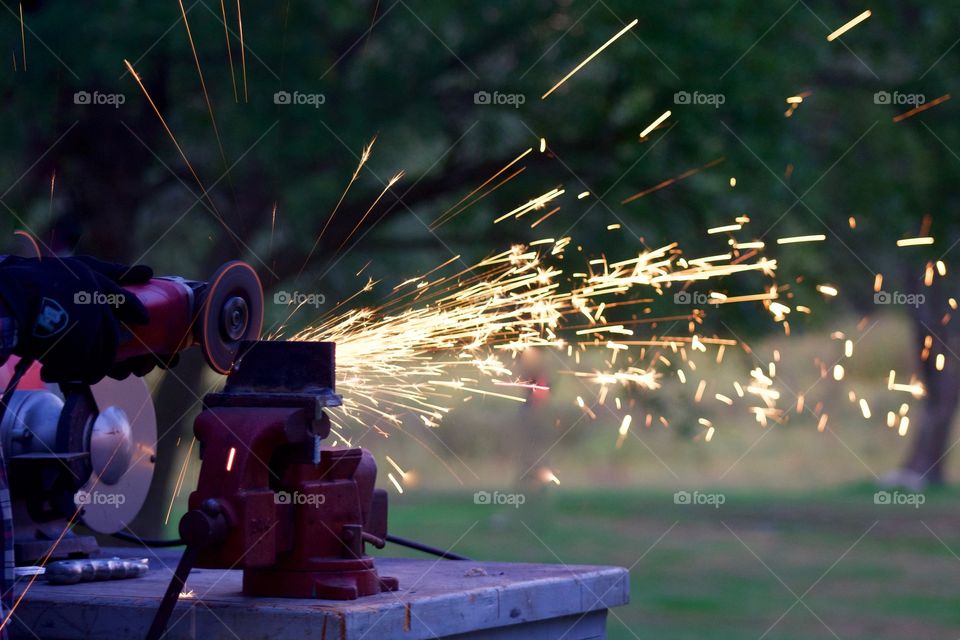 Side view of sparks from a bench grinder being used by a man on a metal part