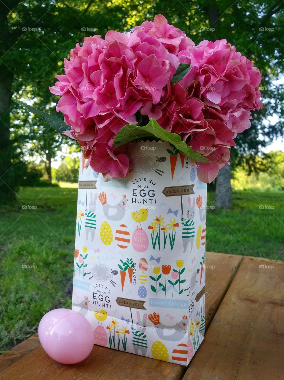 A pink hydrangea in an Easter sack with an egg on a wooden patio in the evening in spring