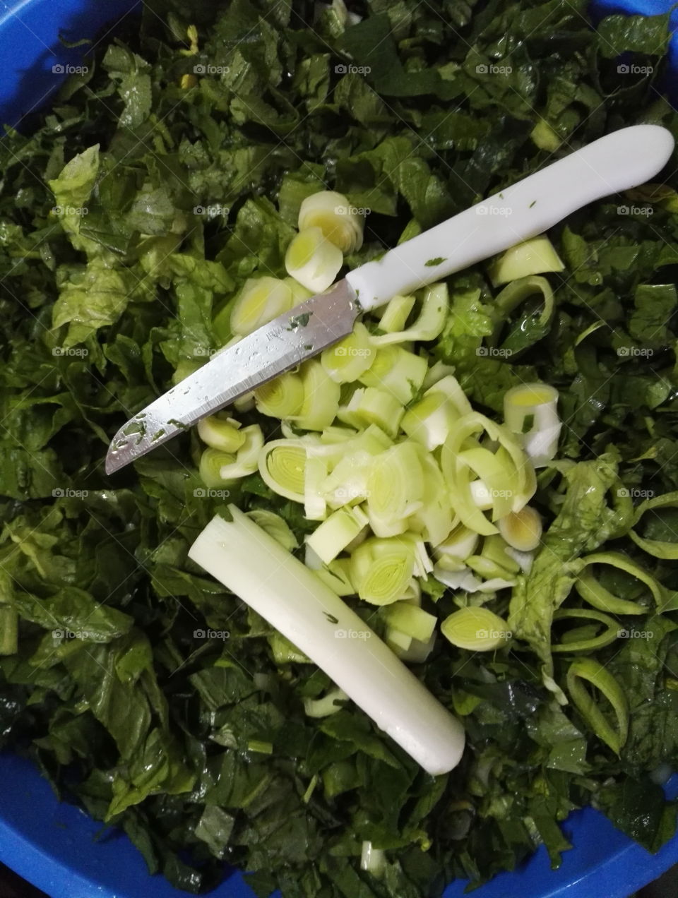 green cut vegetables in a blue bowl with knife