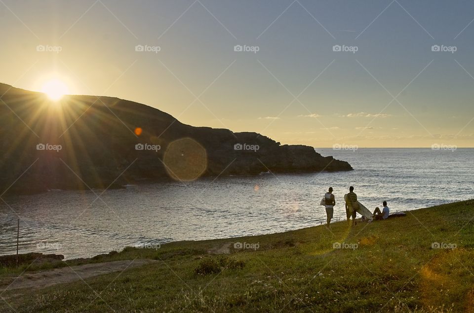 Three young men contemplate the sea on a calm beach at sunset