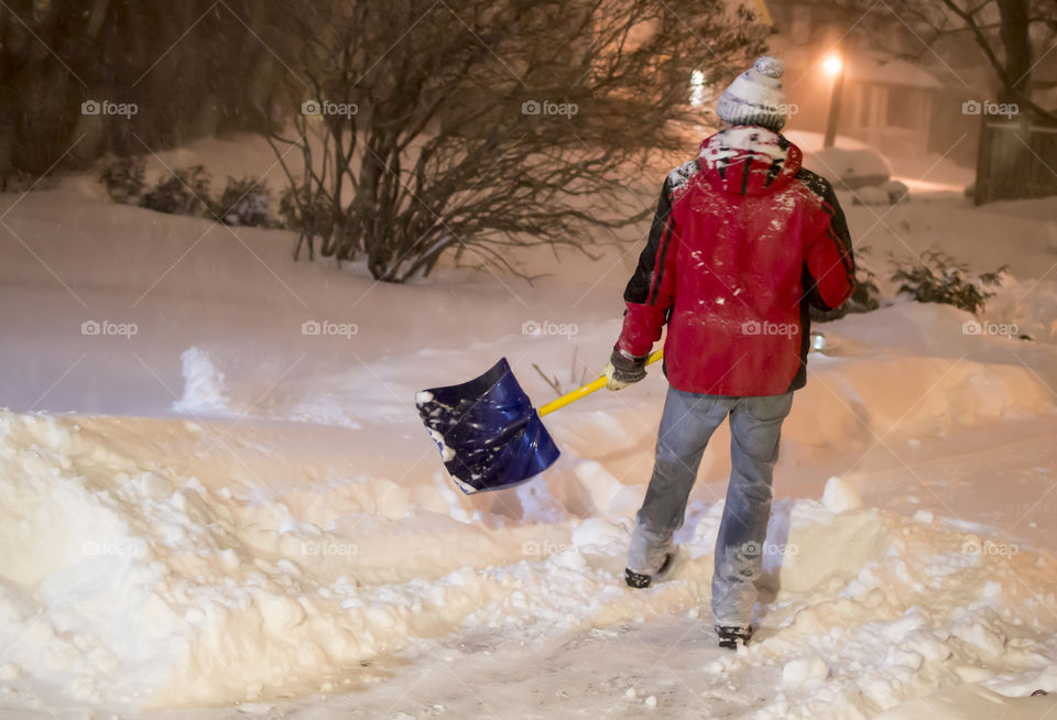 Man shovelling snow during heavy snowfall blizzard in driveway at home 