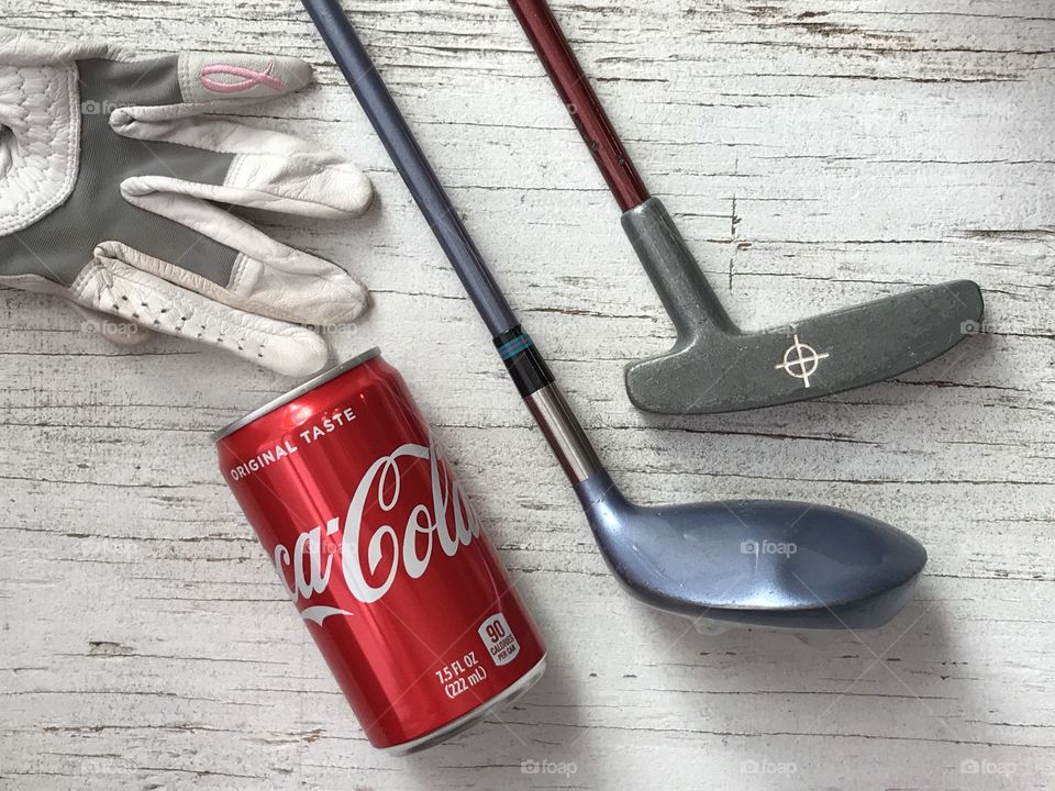 A can of Coca Cola and golf equipment on a rustic white background 