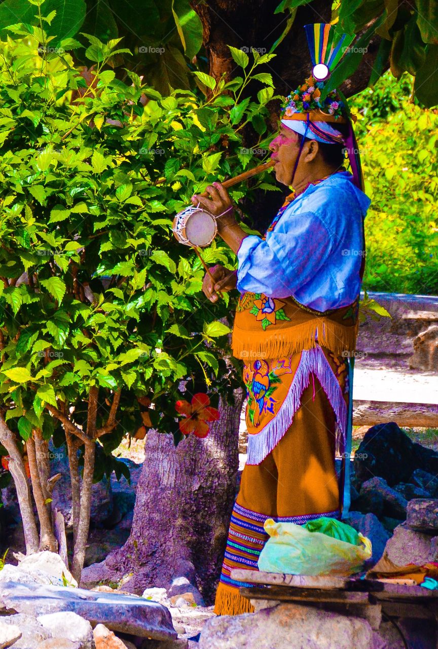 Man dressed in traditional clothing playing instrument while visiting Tulum 