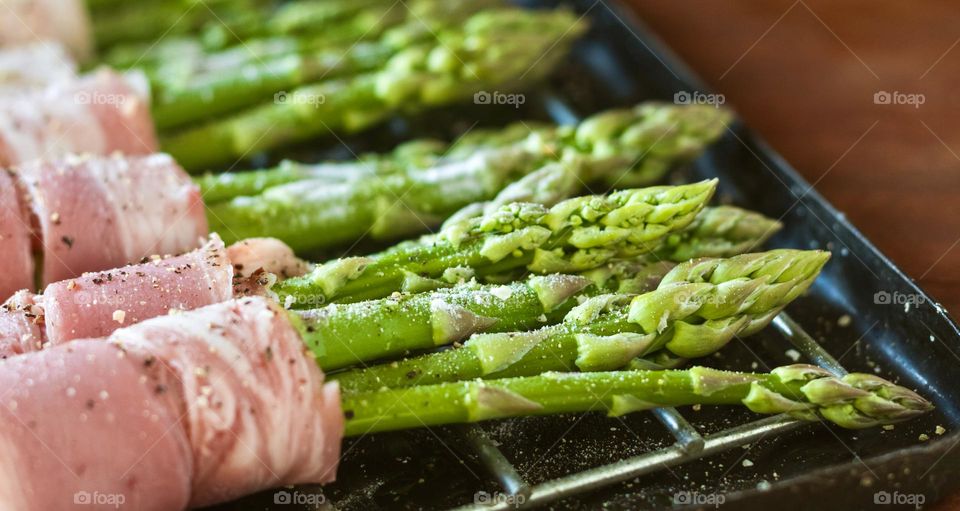 Fresh green asparagus spears, wrapped in bacon and seasoned with salt ready to go under the grill