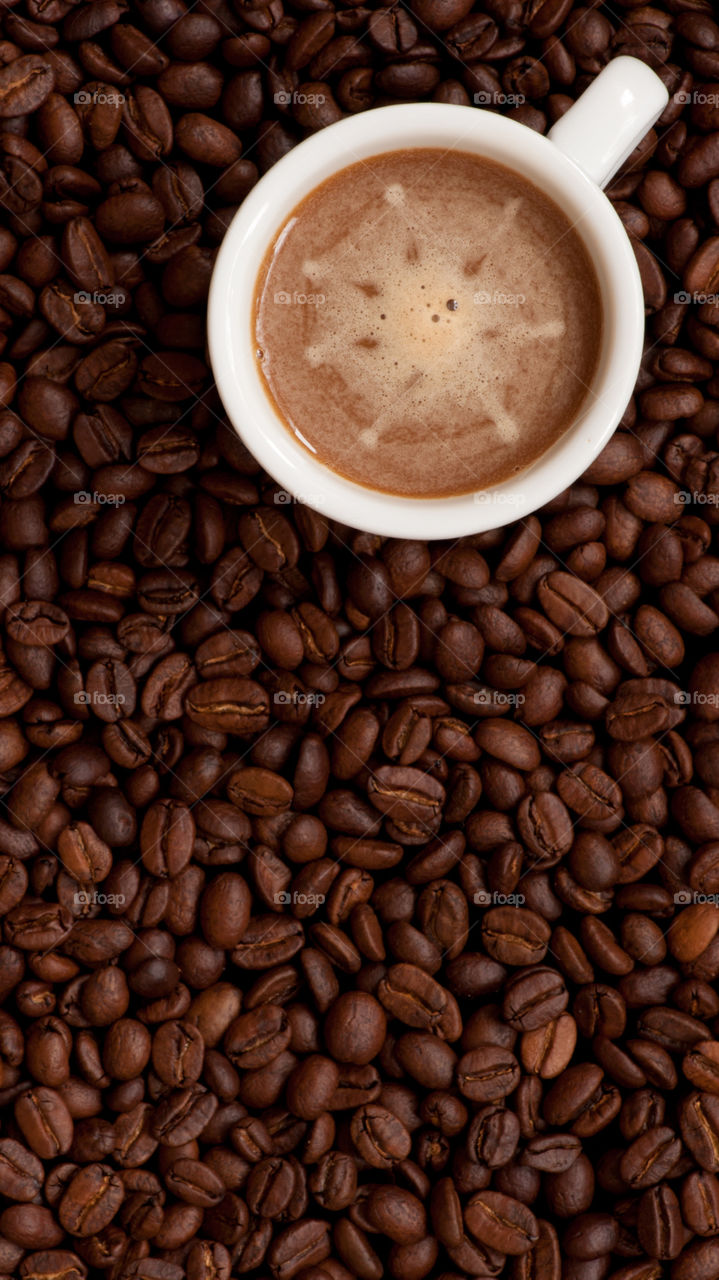 Cup of coffee on coffee beans background, view from above