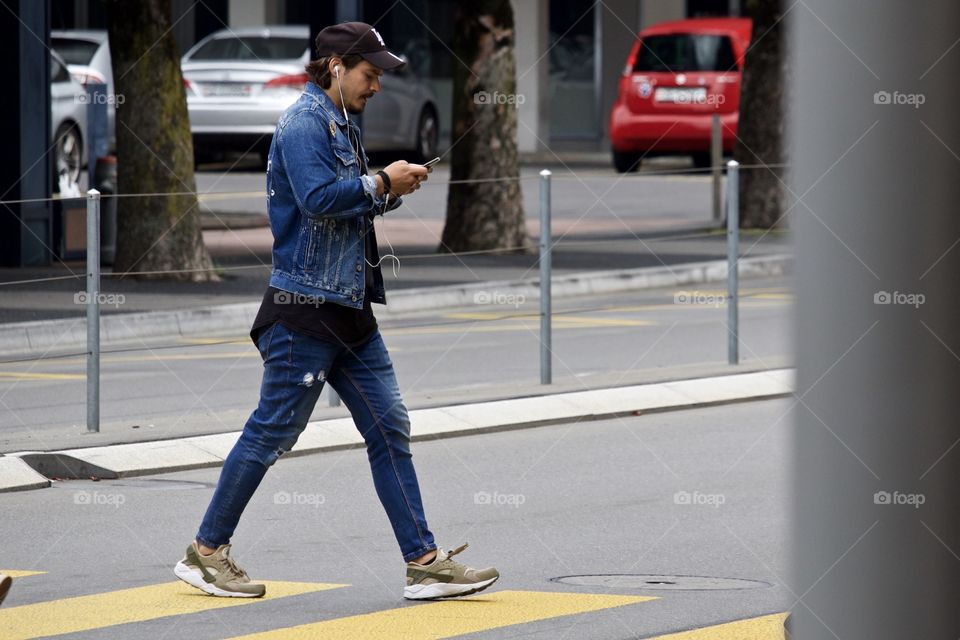 Street Photography.Man texting while crossing the road.
