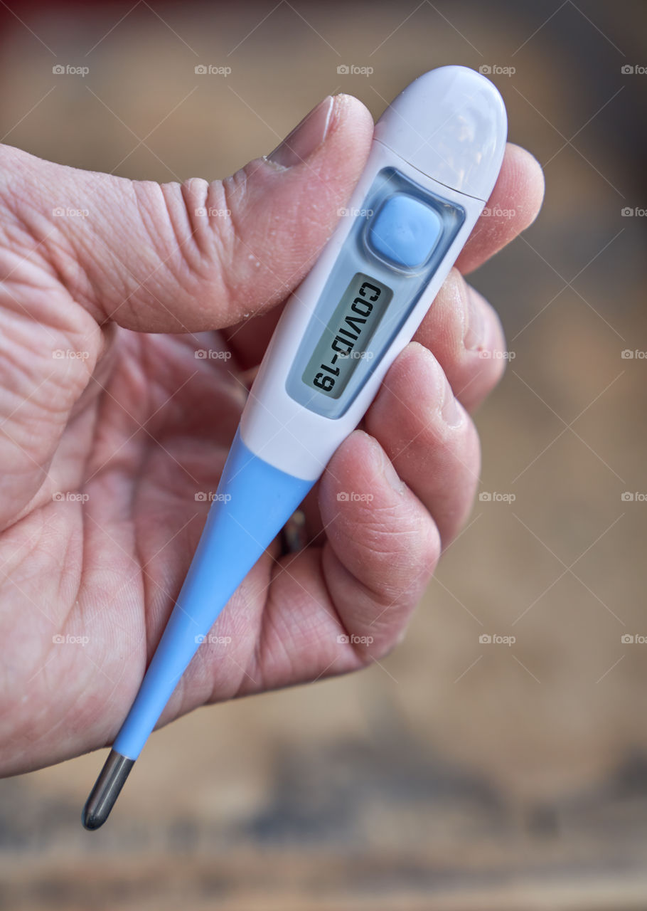 Male hand holds clinical thermometer with covid-19 text on the screen during global covid-19 or corona pandemic.