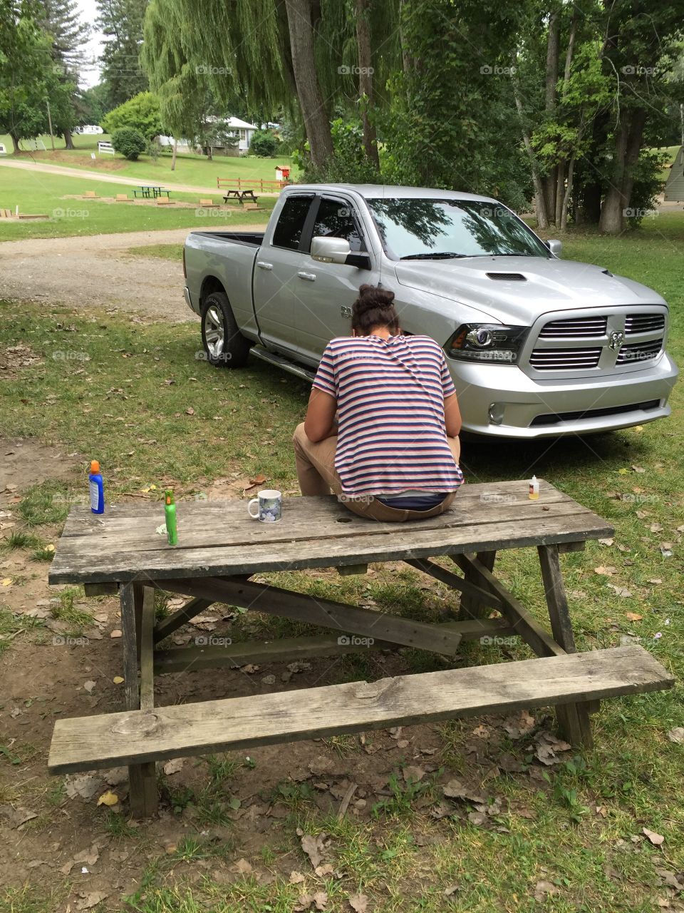 Man sitting  on s picnic  table. With his back showing and  there is a silver. Truck right near him.