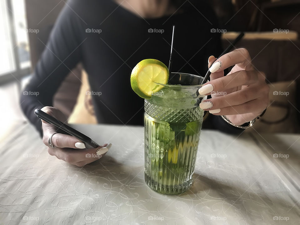 Drinking mojito in the cafe with a mobile phone in hand 