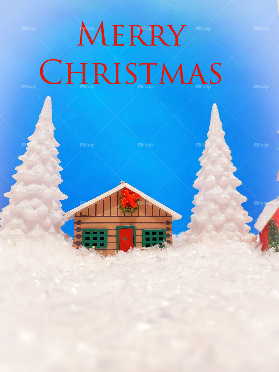 Winter miniature scene of a log cabin and two snow covered pine trees surrounded by snow with the greeting Merry Christmas in red.