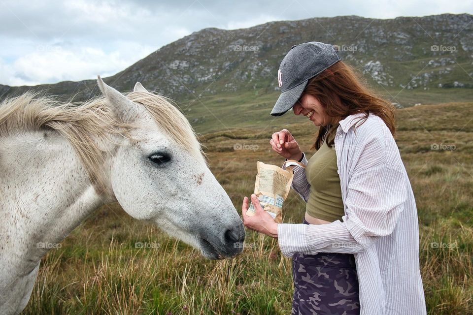 Beautiful young woman feeding white horse at Connemara National park in County Galway, Ireland