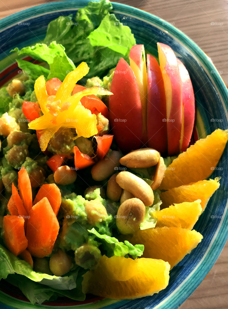 A healthy Vegan salad of lettuce, chick peas, peanuts, carrots, tomato, yellow peppers, orange & apple slices with a garlic lime avocado dressing. Yum!