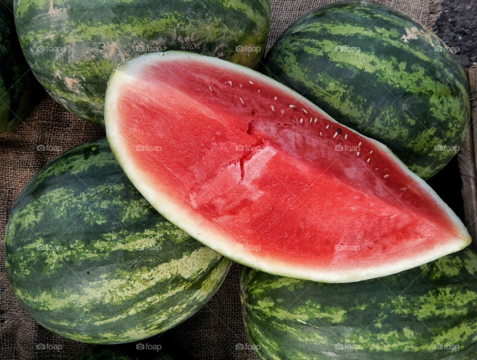 Large Ripe Watermelon Slice Sitting On Group Of Uncut Green Watermelon Fruits