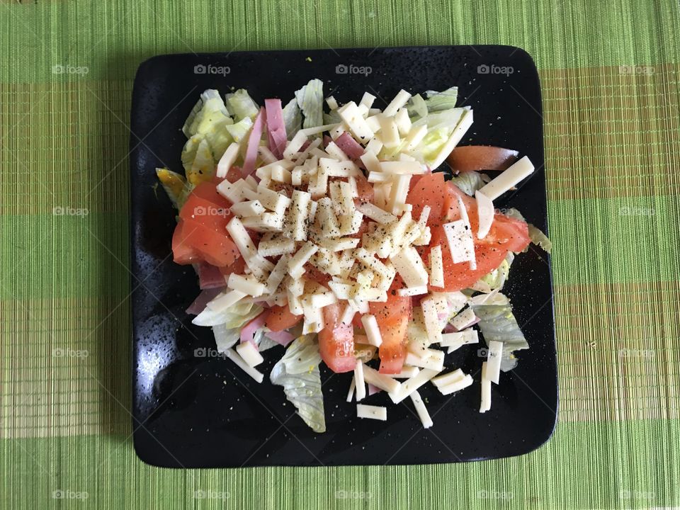 A top view photo of a light and nutritional salad on a black square plate, sitting on a green background.