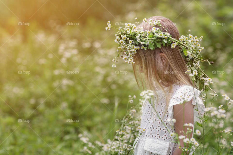 Little girl in flower wreath standing on chamomile field 