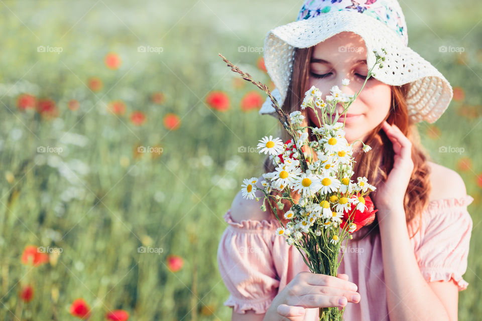 Beautieful young girl in the field of wild flowers. Teenage girl picking the spring flowers in the meadow, holding bouquet of flowers. She wearing hat and summer clothes. Spending time close to nature