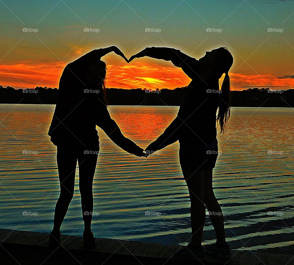 Two girls, best friends making a heart at a magnificent sunset. A show of hands. Even numbers