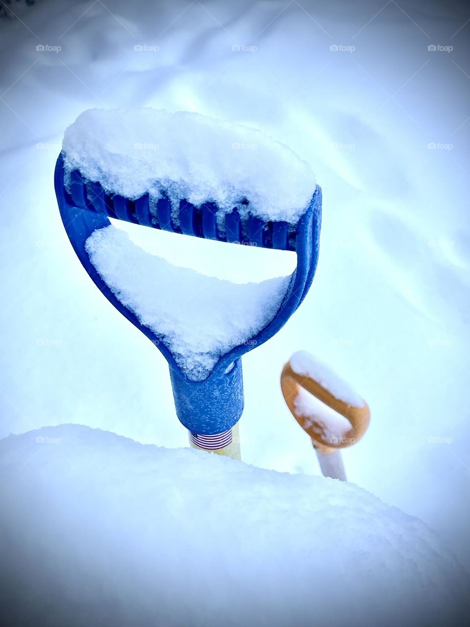 Colorful handles of snow shovels peek over a snow covered railing after a storm.