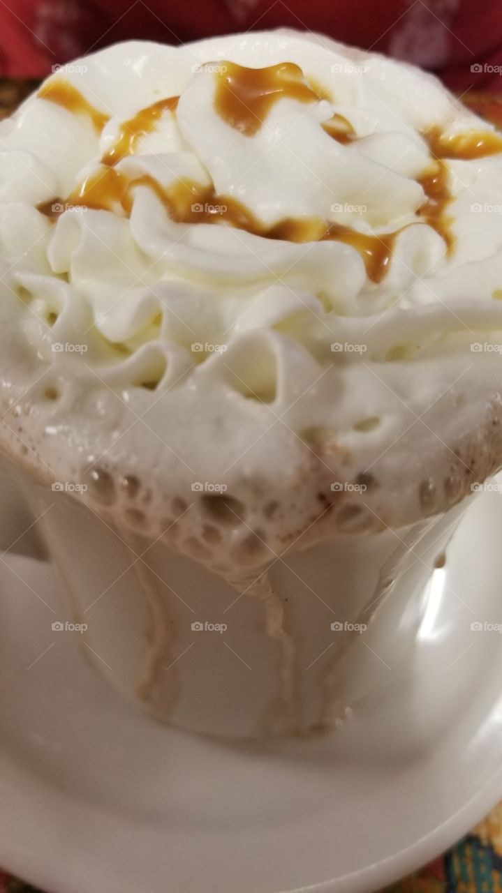 A closeup of a mug filled with hot chocolate with whipped cream and caramel dripping over the sides.