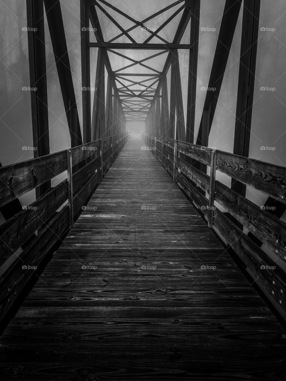 Black and white of an old steel and wood truss footbridge across the lake at Tims Ford State Park in Winchester Tennessee. The dark and foggy ambiance gives it a haunting and mysterious feel. 