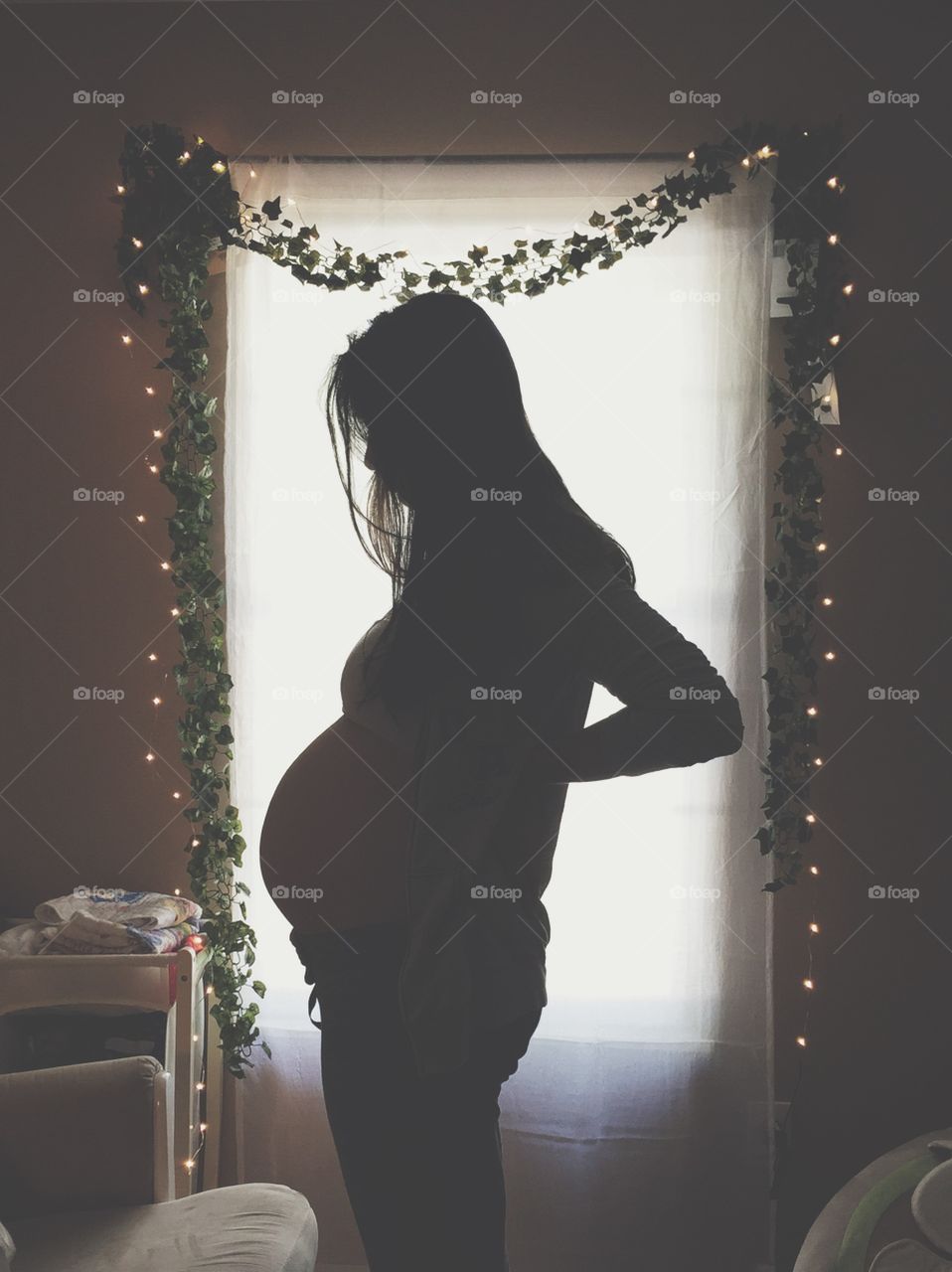 Silhouette of pregnant woman standing in front of decorated curtain