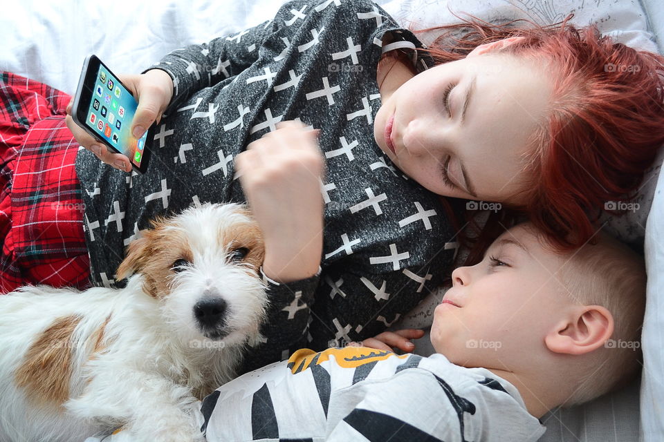 Brother and sister lying on bed with dog holding mobile in hand