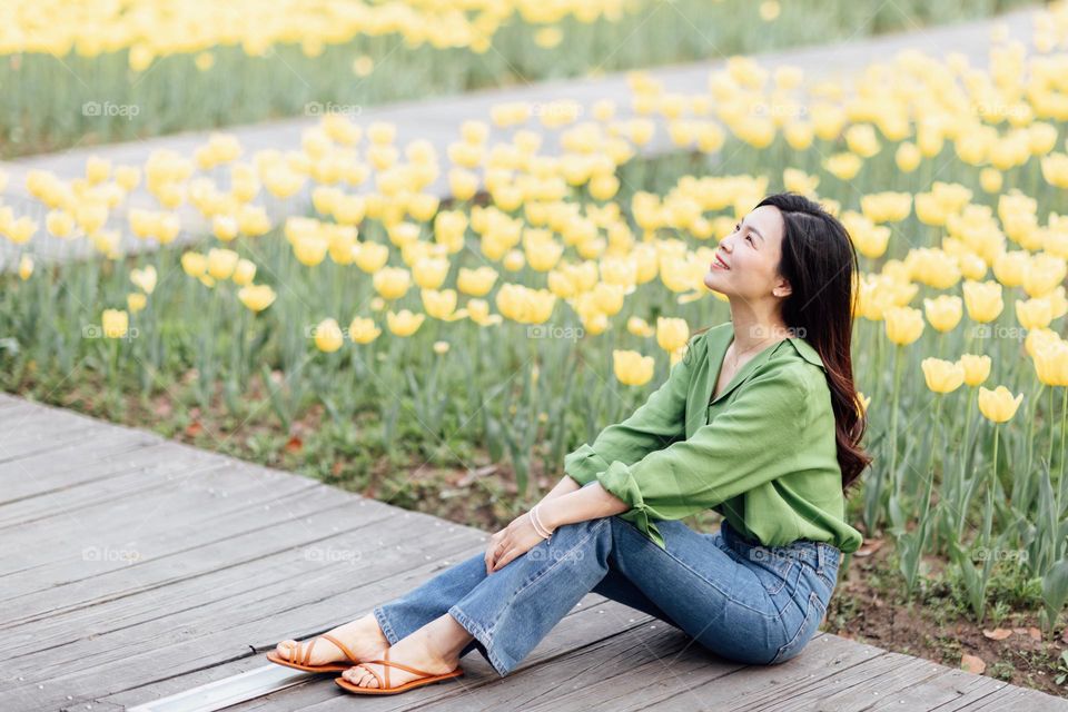 Young woman sitting near yellow tulips field