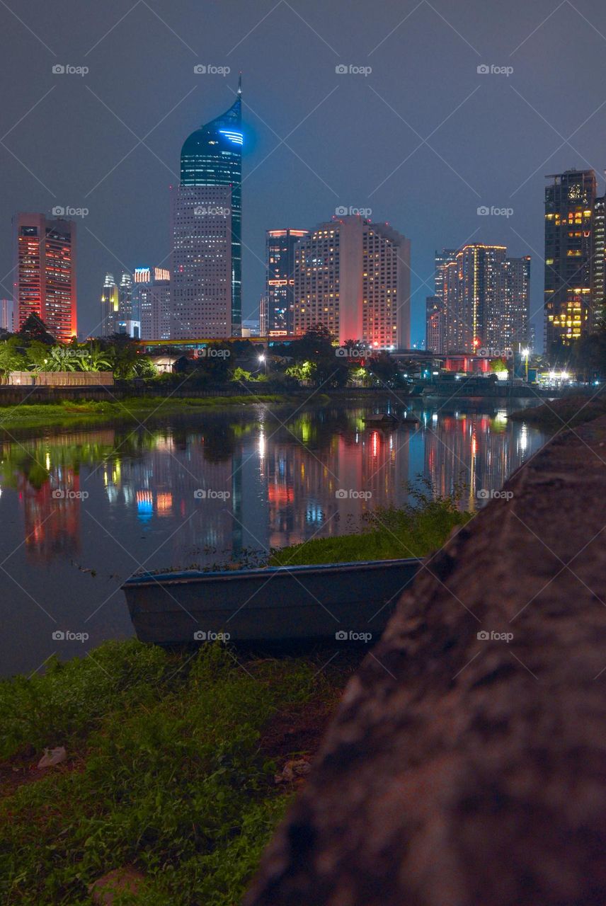 Long exposure photo: A small river flows in the city of Jakarta at night with city lights twinkling