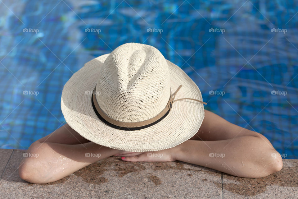 Woman in the hat enjoying sunbathing in the swimming pool in summer